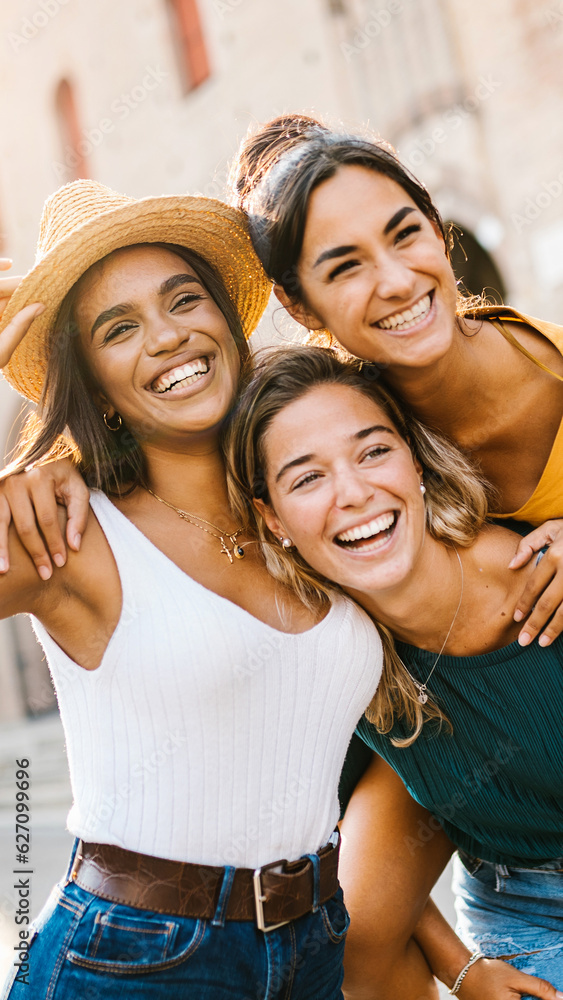 © Xavier Lorenzo - Vertical shot of multiethnic group of three happy young women having fun on summer vacation. Diverse female friends laughing together during their holidays. Female friendship concept.