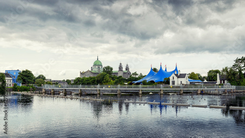 Galway city Cathedral building and blue tent by River Corrib. Dark cloudy sky. Popular town landmark. Dark and moody feel.