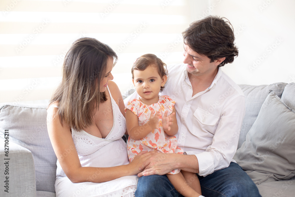 Smiling happy family with the father carrying their little daughter on his lap and pregnant mother Smiling happy family with the father carrying their little daughter on his lap and pregnant mother