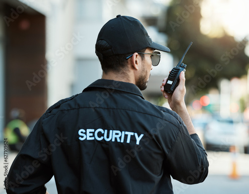 Radio, man and a security guard or safety officer outdoor on a city road for communication. Back of a person with a walkie talkie on urban street to report crime for investigation and surveillance photo