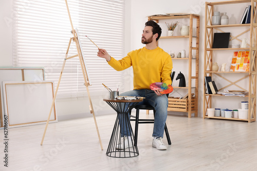 Man painting in studio. Using easel to hold canvas