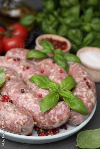 Raw homemade sausages, basil leaves and peppercorns on grey table, closeup