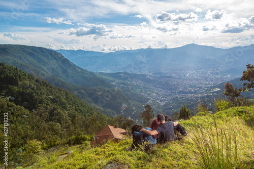 Two people, young couple enjoying a sunny day outdoors, with their dogs, lying in the lush green grass with majestic mountains in the background