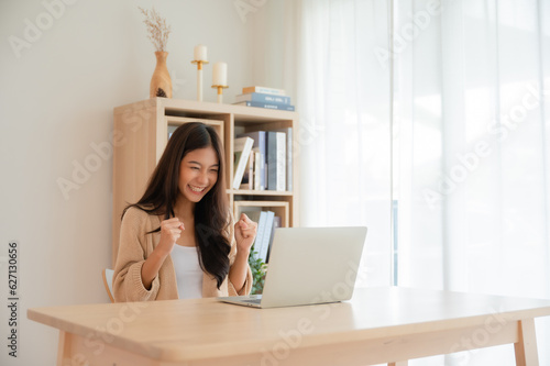 Happy euphoric young asian woman celebrating winning or getting ecommerce shopping offer on computer laptop. Excited happy girl winner looking at notebook celebrating success