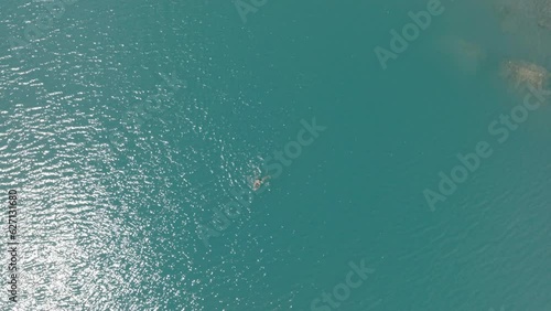 Aerial drone view of man swimming in glacier alpine lake, exploring the Swiss Alps on a sunny day