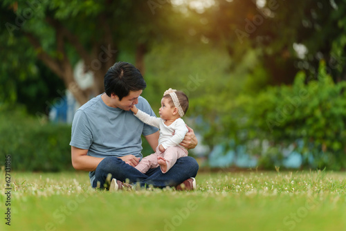 father talking and playing with his infant baby while sitting on grass field