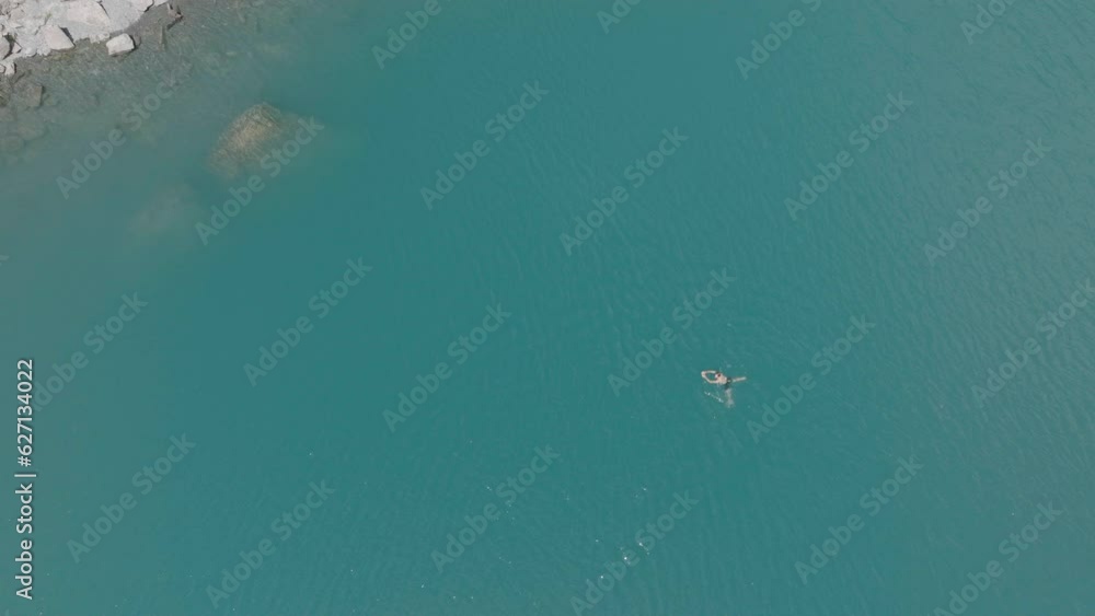 Aerial drone view of man swimming in glacier alpine lake, exploring the Swiss Alps on a sunny day Aerial drone view of man swimming in glacier alpine lake, exploring the Swiss Alps on a sunny day