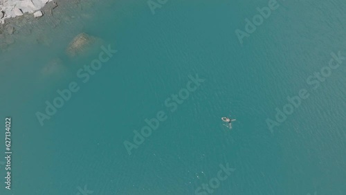 Aerial drone view of man swimming in glacier alpine lake, exploring the Swiss Alps on a sunny day