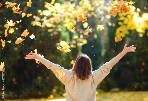 Young woman is having fun while walking through the forest on a sunny autumn day. Girl plays with maple leaves and throws them up. Rustle of leaves.