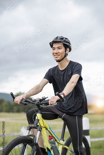 A determined and healthy-fit Asian man in sportswear and a bike helmet rides a bike along country roads. sport, exercise, leisure, summer activity