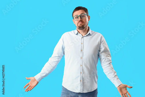 Φωτογραφία Handsome man in stylish eyeglasses shrugging on blue background
