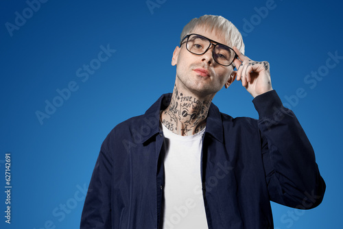 Young tattooed man in eyeglasses on blue background