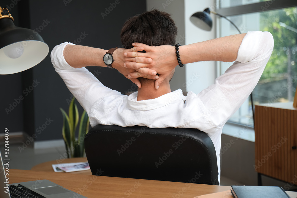 Stylish young man with wristwatch sitting on chair in office, back view