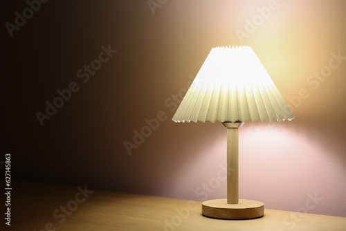 Glowing lamp on wooden table near beige wall in dark room