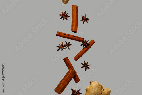 Flying cinnamon sticks, anise stars and ginger root on grey background