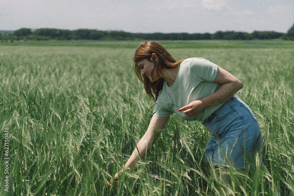 A woman enjoys the fresh air in nature in a green barley field. Summer countryside and gathering flowers. Atmospheric tranquil moment A woman enjoys the fresh air in nature in a green barley field. Summer countryside and gathering flowers. Atmospheric tranquil moment