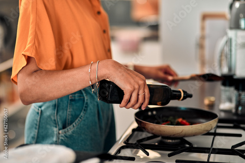 Hands, cooking and olive oil with a woman in the kitchen of her home for food or meal preparation. Stove, pan and container with a female chef in her house to cook for health, diet or nutrition photo