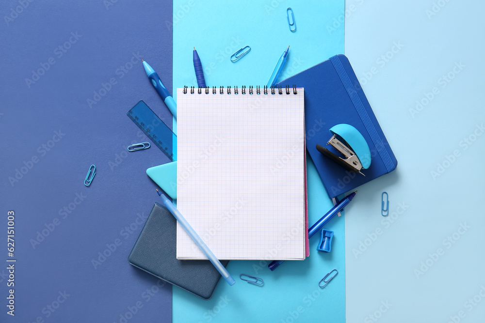 Composition with blank notebook and different school stationery on blue background