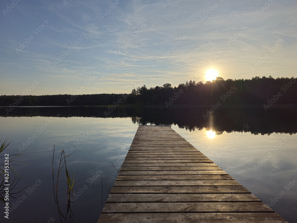 Wooden bridge to a calm lake. Setting sun. Lithuania