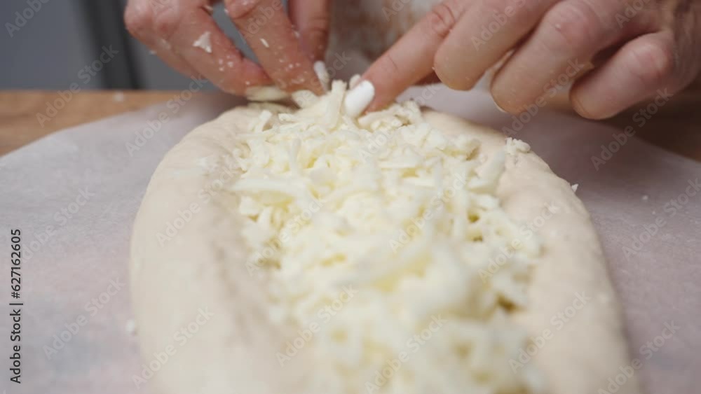 The woman uses her hands to evenly distribute the grated cheese on the Adjaran-style Khachapuri. The scene is captured in slow motion, showcasing a close-up view. The woman uses her hands to evenly distribute the grated cheese on the Adjaran-style Khachapuri. The scene is captured in slow motion, showcasing a close-up view.