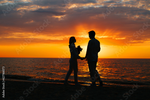 Romance, silhouette boyfriend and girlfriend holding hands together at sea at sunset. Couple in love date on the seashore