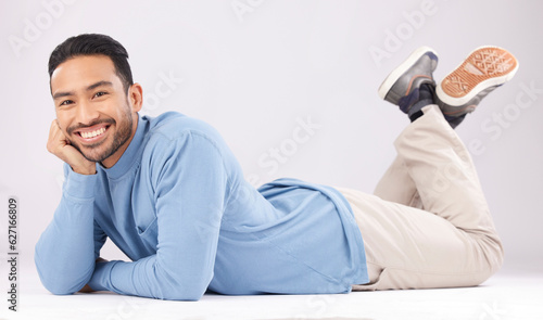 Portrait, happy or Asian man lying on floor isolated on a white background in studio to relax. Friendly smile, calm person or proud male model resting with confidence, fashion or style on the ground © Nadia L/peopleimages.com