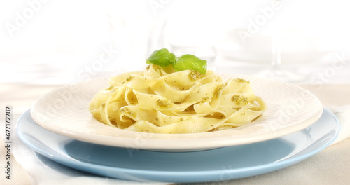 Pasta with pesto on a plate. Serving fettuccine with pesto on a blue background. Italian food with traditional sauce. Mediterranean cuisine. Angle view.