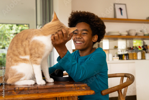 Happy african american boy sitting at table petting his cat