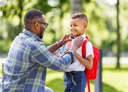 Photo Father escorts happy first-grader boy to school, straightens his bow tie