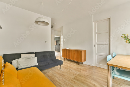 a living room with wood flooring and white walls there is an orange couch in front of the sofas
