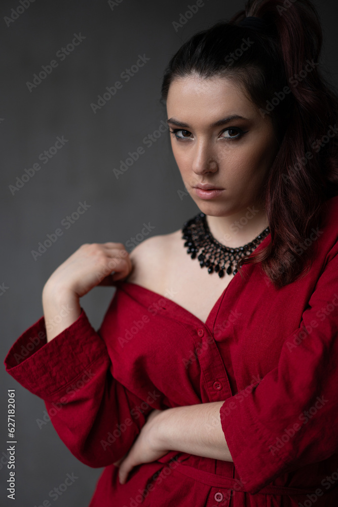 a beautiful young girl in a red shirt with a necklace with a handmade ornament on her neck is posing in a photo studio