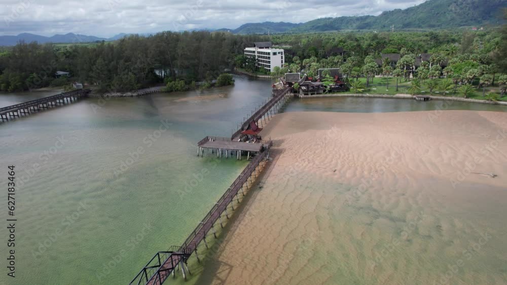 A bridge between two beaches near the ocean. Shallow water. The clear water resembles a river. There are green trees, tropics. The bridge between the hotel and the beach. Clouds in the sky. Thailand A bridge between two beaches near the ocean. Shallow water. The clear water resembles a river. There are green trees, tropics. The bridge between the hotel and the beach. Clouds in the sky. Thailand