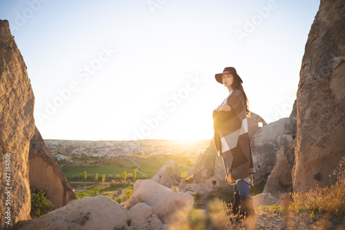 girl hiker in poncho and hat on top of mountain at sunset