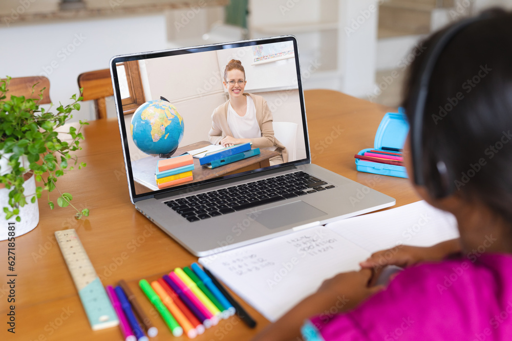 Rear view of biracial girl having a video call with caucasian female teacher on laptop at home Rear view of biracial girl having a video call with caucasian female teacher on laptop at home
