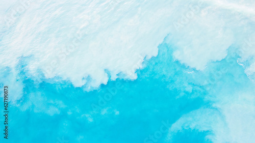 Top view of light blue water with white sand. Waves raise sand and a mix with turquoise water is obtained. Shadows from clouds on a clear ocean. Clear sea. Gradient of blue. The background photo