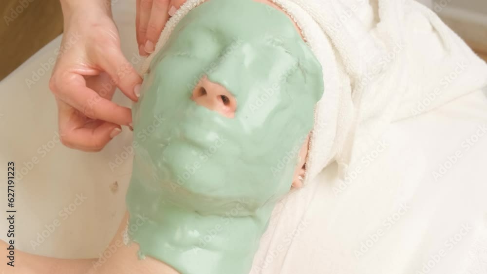 Young woman with face covered with green moisturizing alginate mask in beauty salon. Removal of a cosmetic mask from the face. Young woman with face covered with green moisturizing alginate mask in beauty salon. Removal of a cosmetic mask from the face.