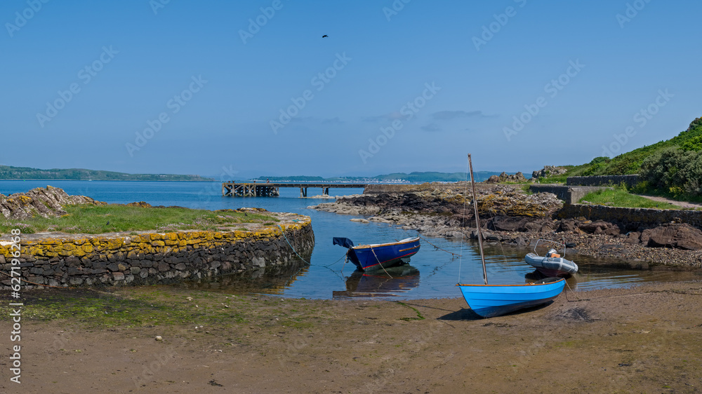 Looking over the rocky harbour  to the old jetty and some small boats at Portencross in Seamill West Kilbride on a bright summers day in June with blue sky and Cumbrae in the distance.