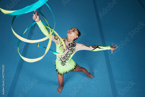 Dance, rhythmic gymnastics and woman in gym with ribbon in air, action with performance top view and fitness. Competition, athlete and female gymnast, creativity and art, routine and energy at arena photo
