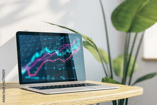 Close up of laptop with forex chart on screen at office workplace with wooden desk, shadows on concrete wall and decor plant. Market, finance and online trading concept. 3D Rendering.