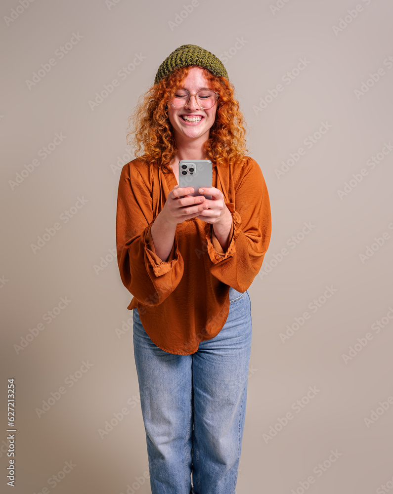 Smiling beautiful woman with curly hair texting over smart phone while standing against background