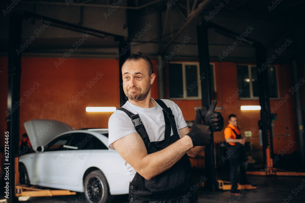 Strong smiling happyfun young male professional technician car mechanic man 20s wear denim blue overalls white t-shirt show ok okay gesture work in light modern vehicle repair shop workshop indoors Strong smiling happyfun young male professional technician car mechanic man 20s wear denim blue overalls white t-shirt show ok okay gesture work in light modern vehicle repair shop workshop indoors
