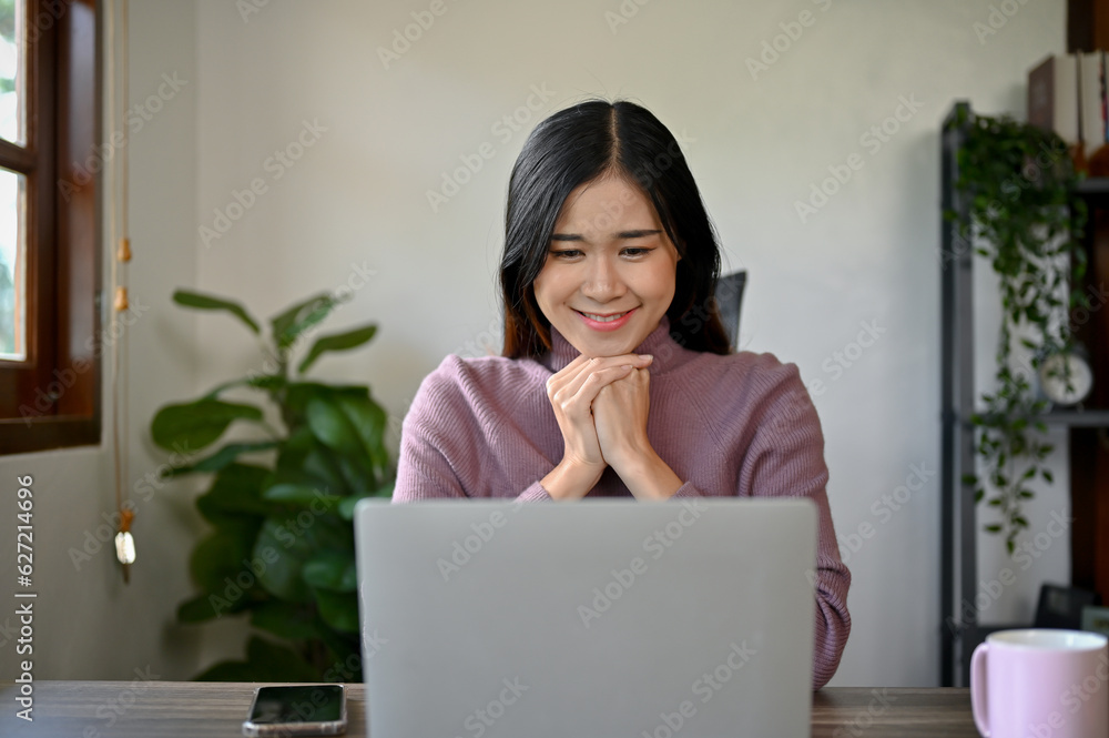 Adorable Asian girl using laptop computer, looking at laptop screen. Relaxing time at her home