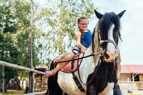 Cute girl on a red horse outdoor. Hippotherapy for young children with down syndrome, therapy after many serious diseases.