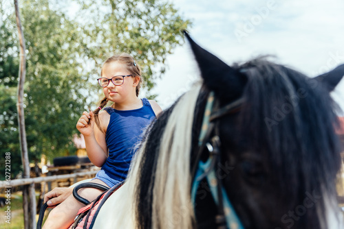 Little cute girl walking with a pony in manege at open air outdoor. Human and horse friendship, hippotherapy and recreation concept.