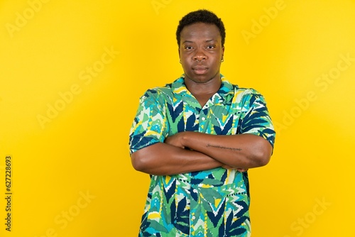 Serious pensive Young latin man wearing hawaiian shirt over yellow background feel like cool confident entrepreneur cross hands.