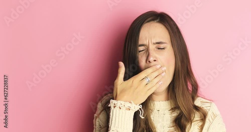 Tired sleepy woman yawns, covers her mouth with hand. Brunette hair girl yawn and cover her mouth, show stop it gesture. Very boring, uninteresting isolated on pink studio background.