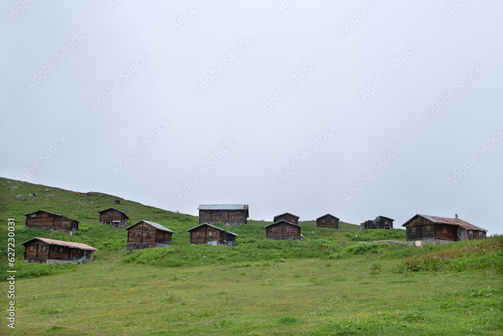 Obraz premium Highland landscape in cloudy and foggy weather. Highland houses made of stone and wood. Wooden plateau houses built on the hill. Wooden plateau houses in Turkey. Sal Plateau Rize Türkiye. 