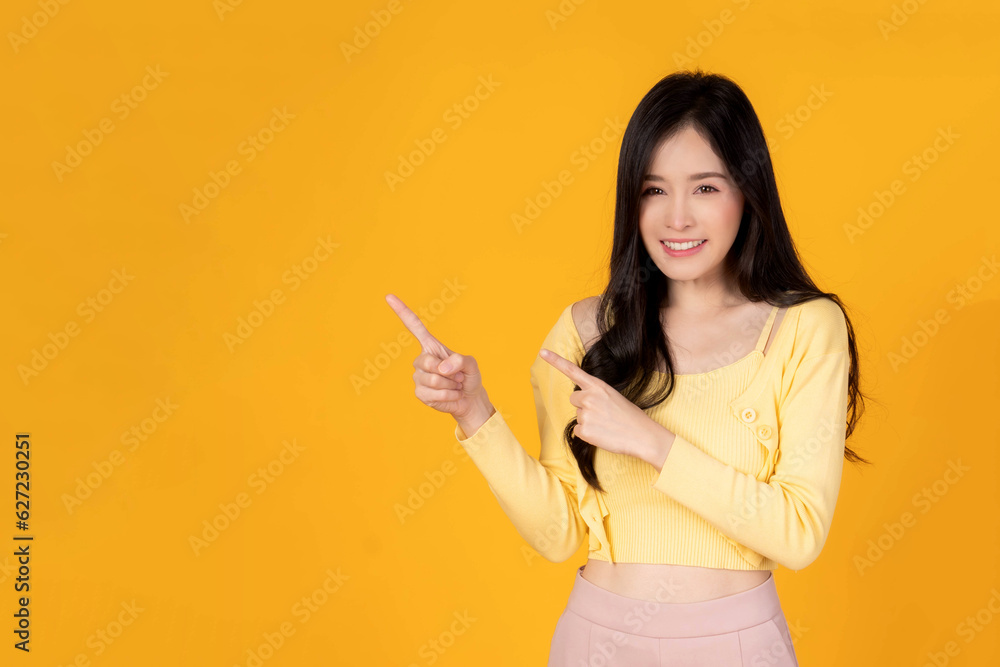 Beautiful Asian woman cute girl in with yellow shirt smiling and pointing finger to empty copy space for present product or blank space for advertising isolated on yellow background Beautiful Asian woman cute girl in with yellow shirt smiling and pointing finger to empty copy space for present product or blank space for advertising isolated on yellow background