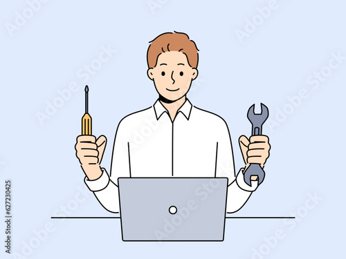 Man repairs laptop after breakdown and holds screwdriver and wrench in hands, working as system administrator. Guy fixes laptop or wants to upgrade by replacing hard drive of computer