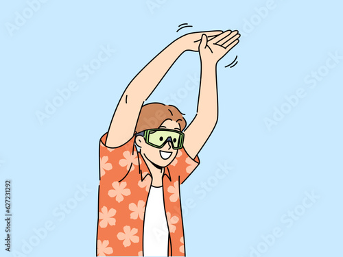 Man tourist stands in pose of swimmer wanting to dive into pool or sea during summer vacation. Young happy guy in goggles for swimming and summer shirt getting ready to jump in sea water